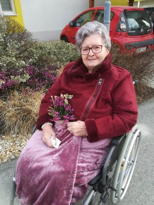 Eine ältere Frau im Rollstuhl hält einen Blumenstrauß und lächelt.
