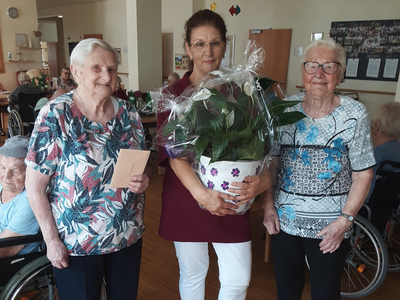 Drei Frauen stehen zusammen, eine hält einen Blumentopf, andere halten eine Karte.