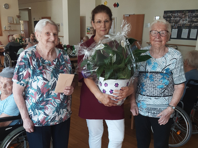 Drei Frauen stehen zusammen, eine hält einen Blumentopf, andere halten eine Karte.