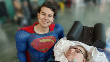 Ein Superman-Kostümträger steht neben einem im Rollstuhl sitzenden Patienten.