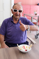 Älterer Mann mit Sonnenbrille gibt Daumen hoch neben einer Schüssel Eis.