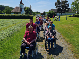 Eine Gruppe von Senioren in Rollstühlen fährt auf einem Weg.