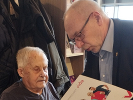 Ein älterer Mensch im Rollstuhl schaut mit jemandem in eine Broschüre.