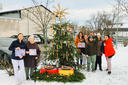Gruppe von Menschen steht um einen festlich geschmückten Weihnachtsbaum im Schnee.
