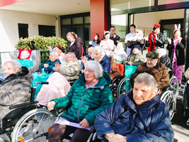 Eine Gruppe älterer Menschen in Rollstühlen bei einer Veranstaltung im Freien.