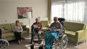 Drei Frauen in einem Wohnzimmer, eine im Rollstuhl, unterhalten sich freundlich.