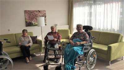 Drei Frauen in einem Wohnzimmer, eine im Rollstuhl, unterhalten sich freundlich.