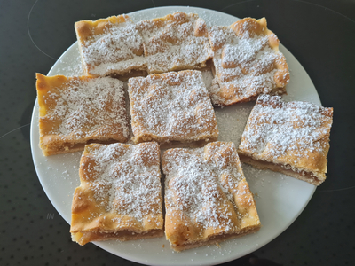 Ein Teller mit acht rechteckigen Kuchenstücken, bestreut mit Puderzucker.