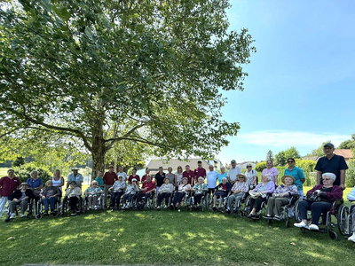Gruppe von Menschen in Rollstühlen, versammelt im Freien unter einem Baum.