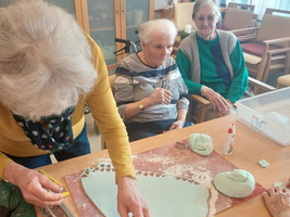 Ältere Frauen gestalten bunte Dekorationen aus Modelliermasse am Tisch.