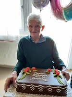 Ein älterer Mann sitzt vor einer Geburtstagstorte mit Rosen.