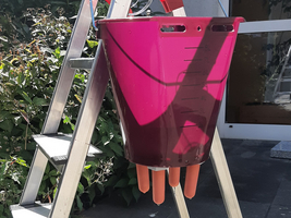 Ein rosa Eimer hängt an einer Leiter, daneben ein Glasbehälter.