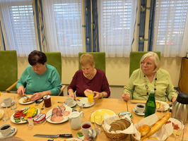 Drei ältere Frauen genießen ein gemeinsames Frühstück an einem gedeckten Tisch.