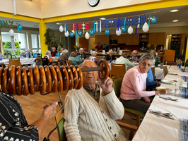 Eine Gruppe älterer Menschen genießt ein Festessen mit Brezeln in einem Speisesaal.