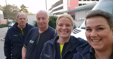 Vier Personen in Uniform lächeln in die Kamera vor einem Gebäude.