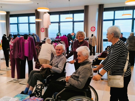 Vier ältere Frauen, darunter zwei im Rollstuhl, in einem Bekleidungsgeschäft.