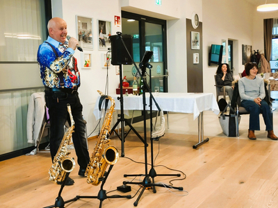Ein Mann mit buntem Hemd singt, während zwei Saxophone neben ihm stehen.