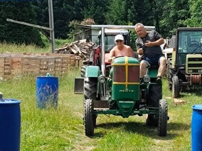 Zwei Personen fahren gemeinsam auf einem Traktor durch eine grüne Wiese.