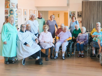 Eine Gruppe älterer Menschen, einige im Rollstuhl, posiert in einem Gemeinschaftsraum.