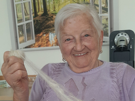 Eine ältere Frau hält stolz eine weiße Wollfaser in der Hand.