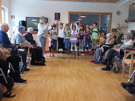 Kinder führen eine Darbietung vor Senioren in einem Gemeinschaftsraum auf.