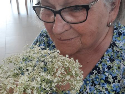 Eine ältere Frau mit Brille hält einen strauß weißer Blumen in der Hand.