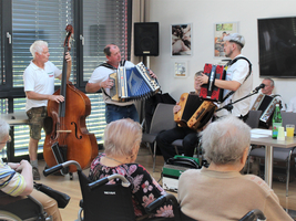 Musiker spielen verschiedene Akkordeons und Kontrabass vor Publikum in einem Raum.