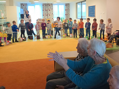 Kinder singen und spielen Musik vor älteren Menschen in einer Einrichtung.