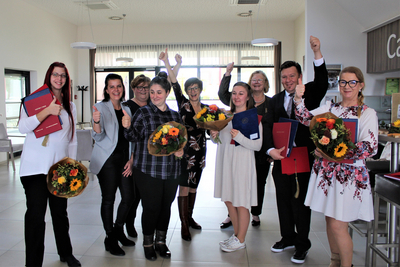 Gruppensieger feiern mit Blumensträußen und Daumen hoch in einem modernen Raum.