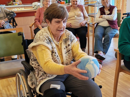 Eine Frau im Rollstuhl spielt mit einem Ball in einer Gruppe älterer Menschen.