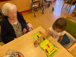 Eine ältere Frau spielt mit einem kleinen Mädchen ein Brettspiel am Tisch.
