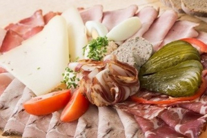 Ein Teller mit verschiedenen Wurstsorten, Käse, Pickles und Tomaten.