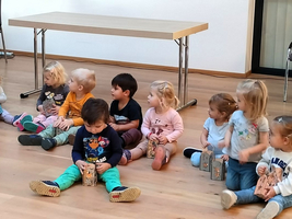 Kinder sitzen im Halbkreis und halten kleine Kisten in den Händen.