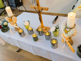 Eine Tischdekoration mit Kerzen, Blumen und einem Kreuz als zentrale Elemente.