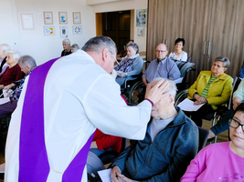 Ein Priester segnet einen älteren Mann in einer Gruppe von Senioren.