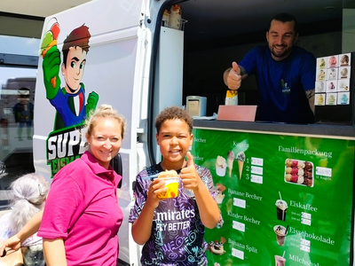 Ein Junge hält ein Eis und lächelt, während eine Frau neben ihm steht.