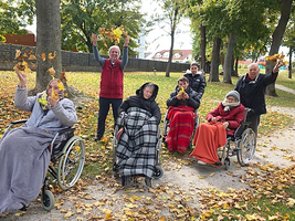 Sechsergruppe im Freien hält bunte Herbstblätter in Rollstühlen.