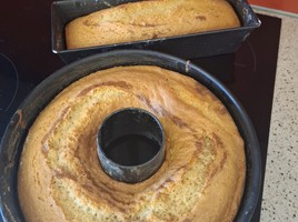 Zwei frisch gebackene Kuchen in runden und rechteckigen Formen auf einer Arbeitsfläche.