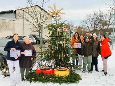 Gruppe von Menschen vor einem geschmückten Weihnachtsbaum im Schnee.