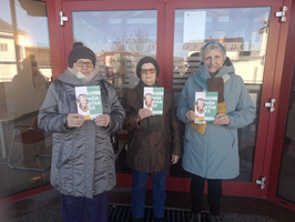 Drei ältere Frauen halten Informationsflyer vor einer Glasfront.