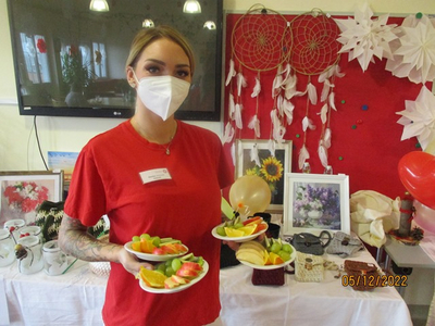 Eine Person in Maske hält zwei Teller mit frischem Obst.