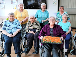 Eine Gruppe älterer Frauen in Rollstühlen mit einem bunten Salat.