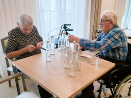 Zwei Senioren sitzen an einem Tisch und arbeiten mit Flaschen.