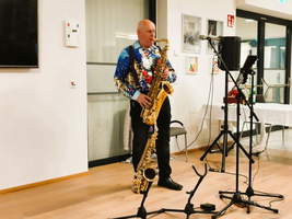Ein Mann spielt Saxophon auf einer Bühne in festlicher Kleidung.