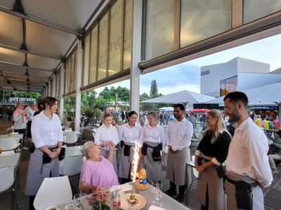 Eine Gruppe von Kellnern feiert mit einer älteren Dame ihren Geburtstag.