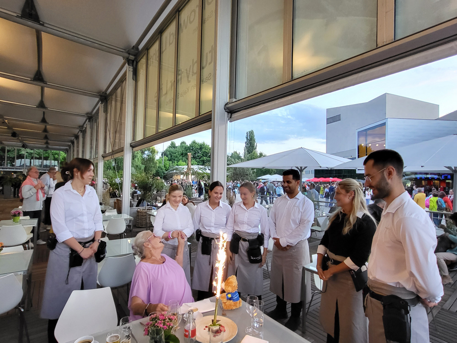 Eine Gruppe von Kellnern feiert mit einer älteren Dame ihren Geburtstag.