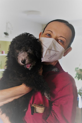 Eine Frau mit einer Maske hält einen schwarzen Welpen in den Armen.