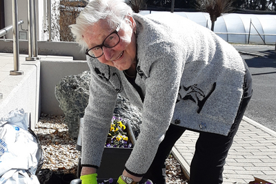 Eine ältere Frau pflanzt Blumen in Pflanzkästen im Freien.