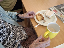 Eine ältere Person genießt Kuchen und eine Tasse Kaffee am Tisch.