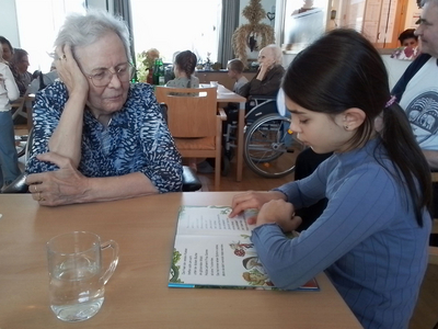 Ein kleines Mädchen liest einer älteren Frau in einem Gemeinschaftsraum vor.